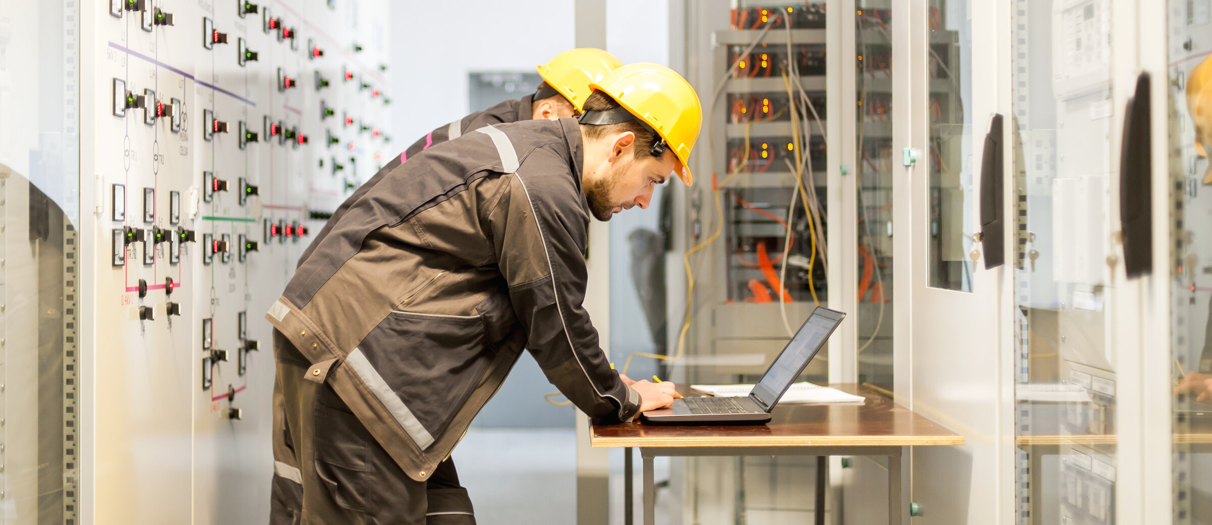 Two maintenance engineers inspect relay protection system with laptop comp