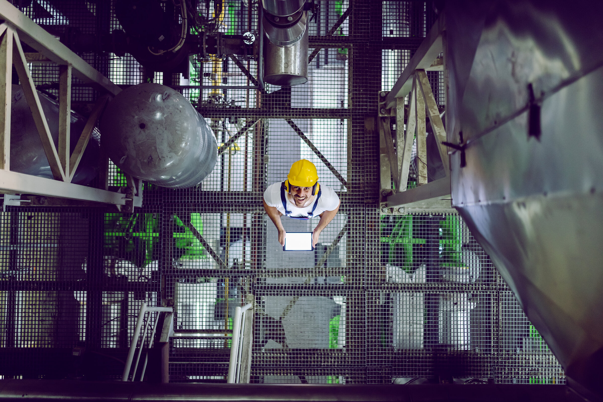 Top view of smiling plant worker in protective clothing using ta