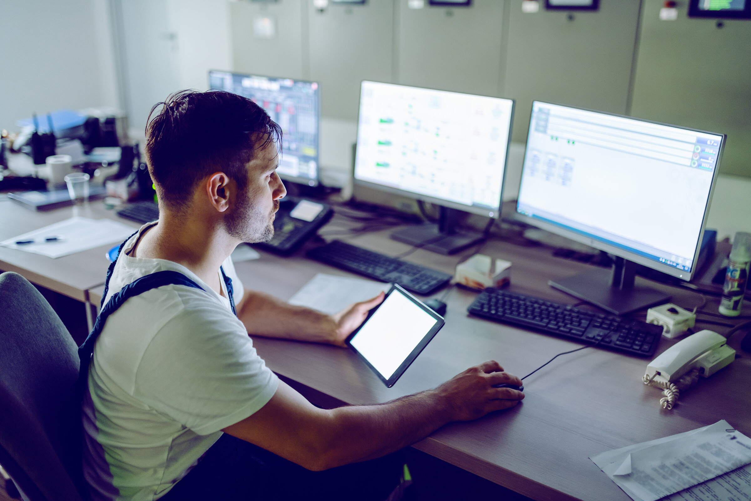 Hardworking plant worker sitting in control room, holding tablet